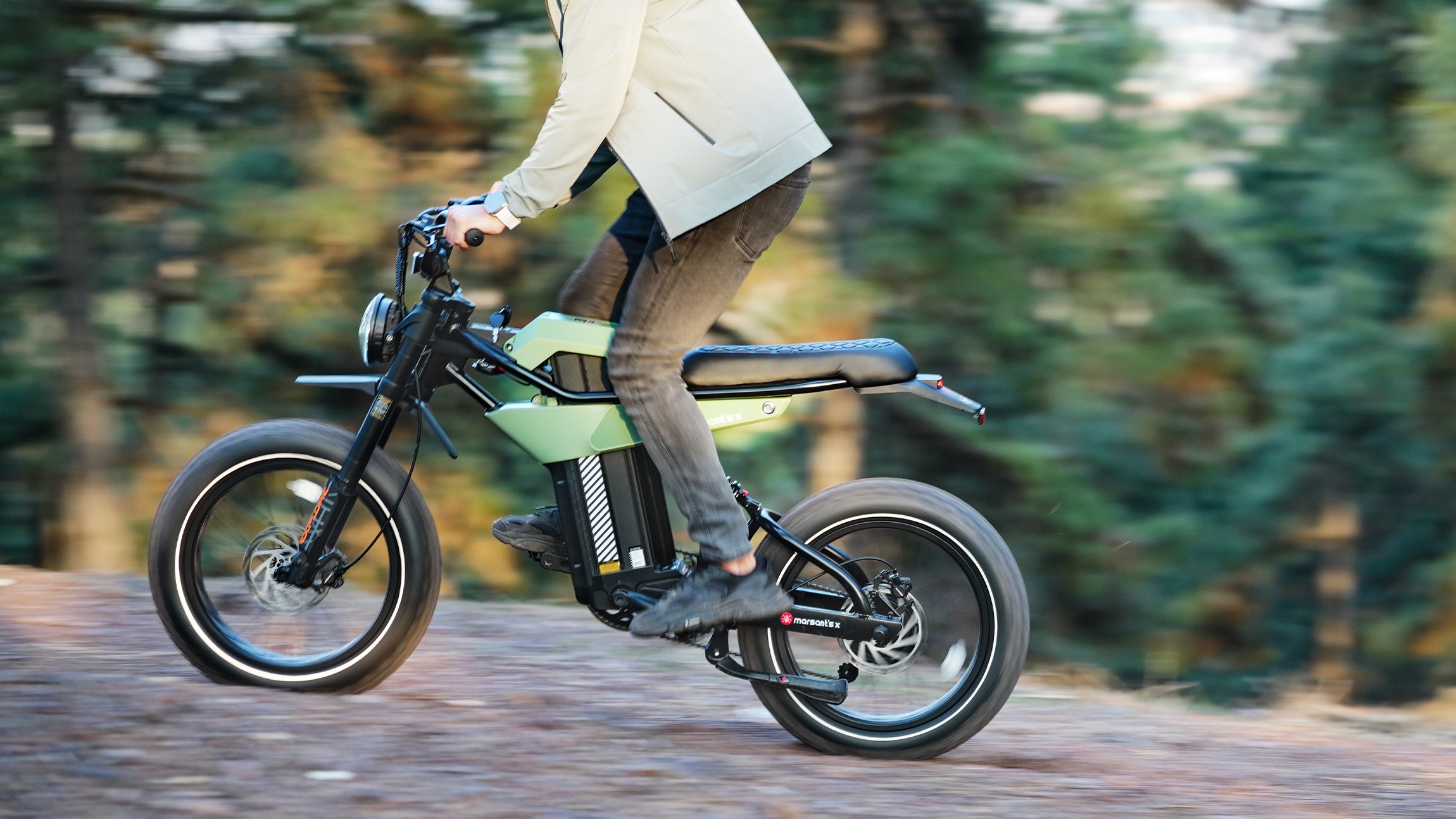 A person rides a green electric bike with large tires on a forest trail, enjoying the scenic surroundings.
