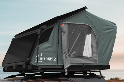 A close-up of Intrepid's Geo 2.5 rooftop tent on top of a vehicle near the ocean. The tent is a clamshell style tent modified with a hinged roof to increase space inside the tent.  