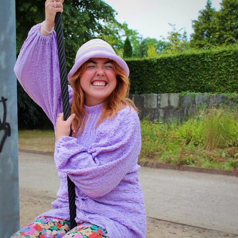 Ung glad kvinde iført en lilla solhat fra genbrug