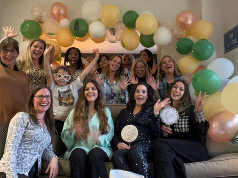Group of women smiling for photo at a baby shower with a balloon arch behind them.