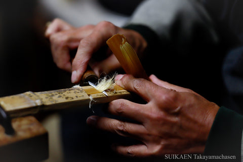 Bamboo being shaved with a knife to make finer prongs 