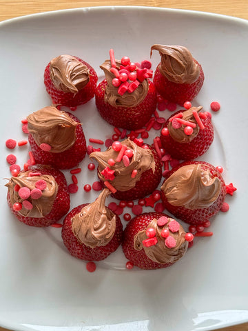 A white plate of strawberries topped with whipped dark chocolate honey ganache and red sprinkles