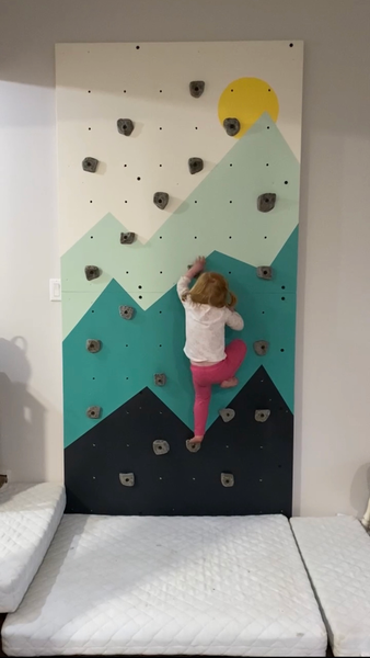 Little girl bouldering on home rock climbing wall
