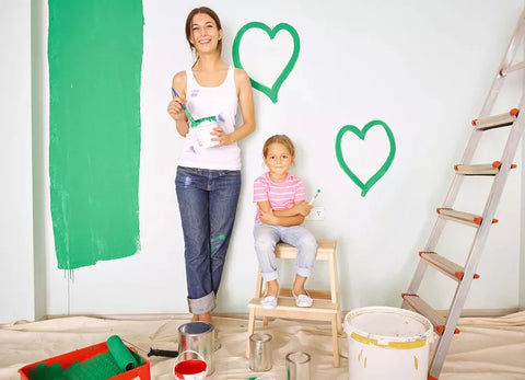 mom and young daughter stand beside wall being painted in green