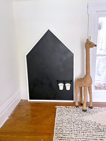 house shaped kids chalk wall standing beside a giraffe toy on a rug