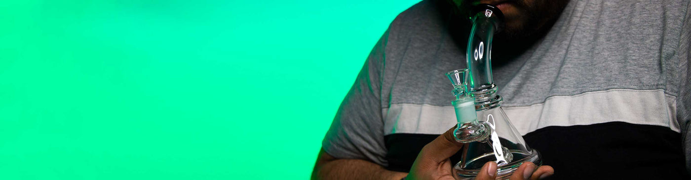 Man inside studio with green lighting using glass water pipe