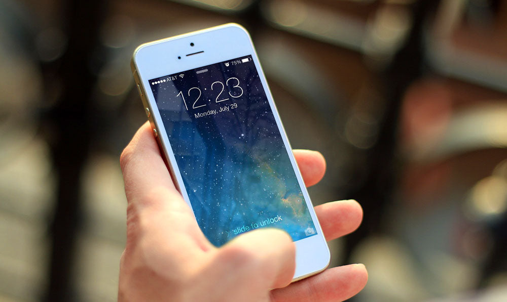 Person holding white smartphone in front of trees