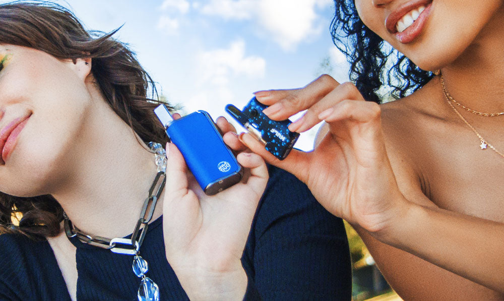 Two women holding Wulf Mods Duo and Micro Plus at a park under clouds with natural lighting