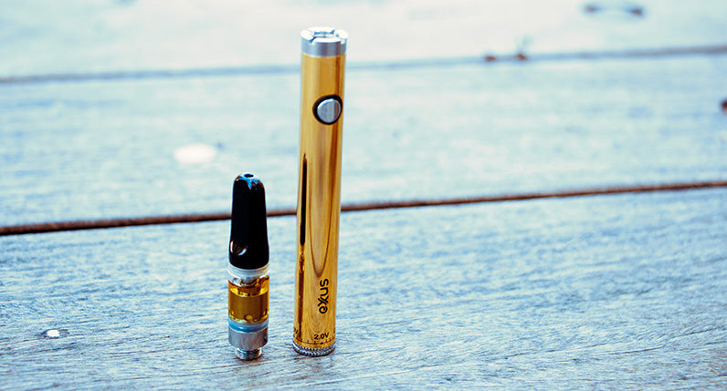 Gold Exxus Twistr with oil cartridge standing on a wooden table at park