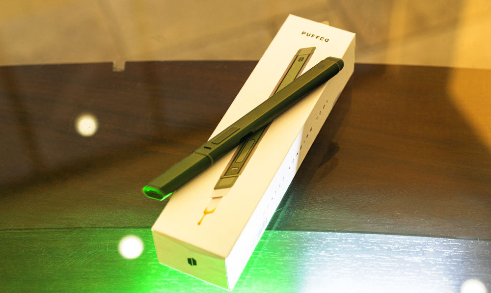 Puffco Hot Knife resting on top of packaging on wooden table with green and white lighting from underneath
