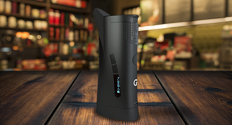 G Pen Roam Vaporizer standing on wooden table in coffee shop.