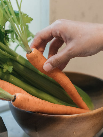 Eine Hand greift nach Karotten, die in einer Schale liegen.
