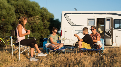 family grouped together in a field sitting on camping chairs with an RV in the background