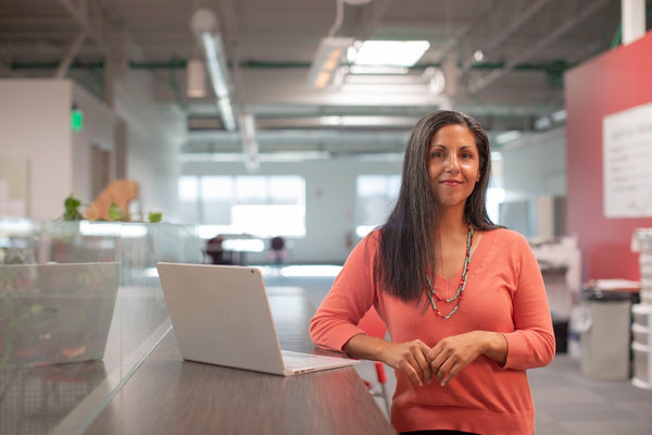 A woman experiencing the menopause transition while standing at work with a laptop.