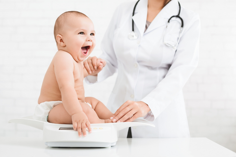 Ein Baby sitzt beim Arzt auf einer Waage