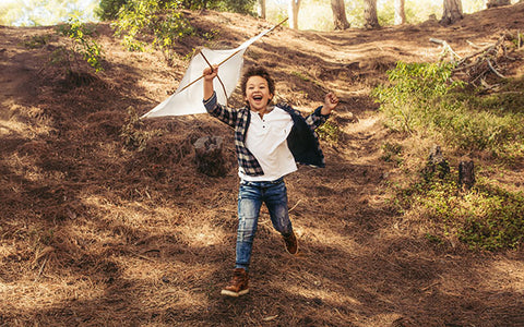 Kleiner Junge rennt mit Flugdrachen in der Hand den Berg hinunter