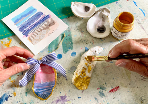 Karin's hands holding an ornament while her mother paints one of the oyster shells gold