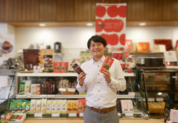 Saito san from Ragueneau Sasaki posing with two Pporo Chocolat snacks in Ragueneau's Main Shop in Japan