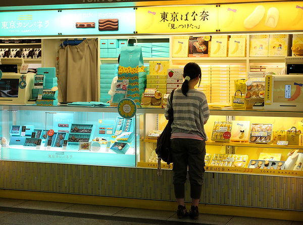 A Japanese commuter in Tokyo Station choosing a package of Tokyo Banana from brightly colored shops.