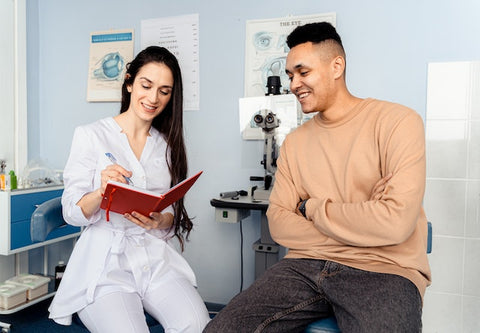 Eine Augenärztin und ihr Patient sitzen im Untersuchungsraum und blicken in ein Heft, dass die Ärztin in der Hand hält.