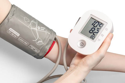 Ein Blutdruckmessgerät mit Schlauch und Manschette ist an einem Arm befestigt. Das Display zeigt die Messwerte an.