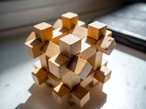 Ein Steckspiel aus Holz. Verschiedene Bauteile sind so ineinander gesteckt, dass sie einen Würfel bilden, an dessen Ecken drei der Einzelteile überstehen.
