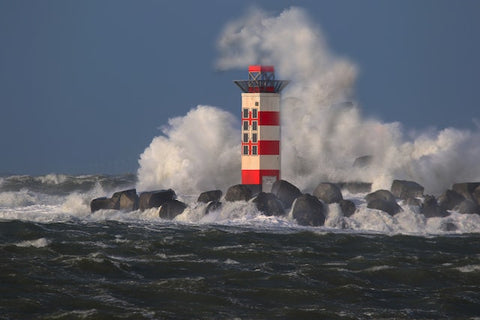 Ein Leuchttum mit roten und weißen Streifen steht auf einem Wellenbrecher. Die aufgewühlte See spritzt bis über den Leuchtturm.