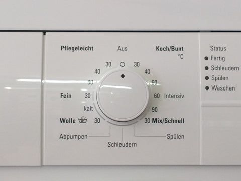 Programmwahlschalter einer Waschmaschine. Auf dem Knopf befindet sich ein dunkler Punkt der die Einstellung anzeigt. Um den Knopf herum befinden sich Zahlen und Programmbezeichnungen.