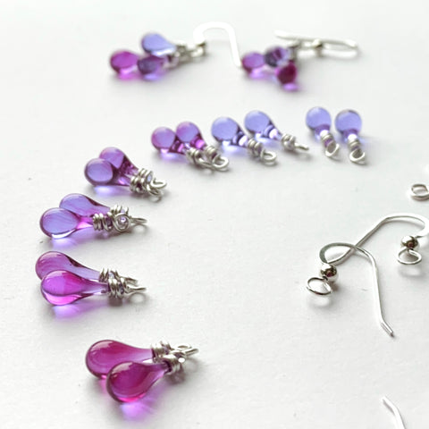 Pairs of magenta and lavender Sundrops ready to be made into Napa Earrings, with Amador Earrings in the background - Pinot Noir color gradient.