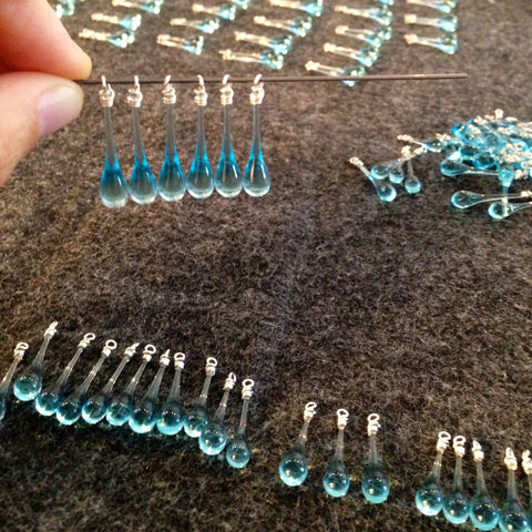 Sorting and pairing glass drops to make glistening, pale blue rain jewelry