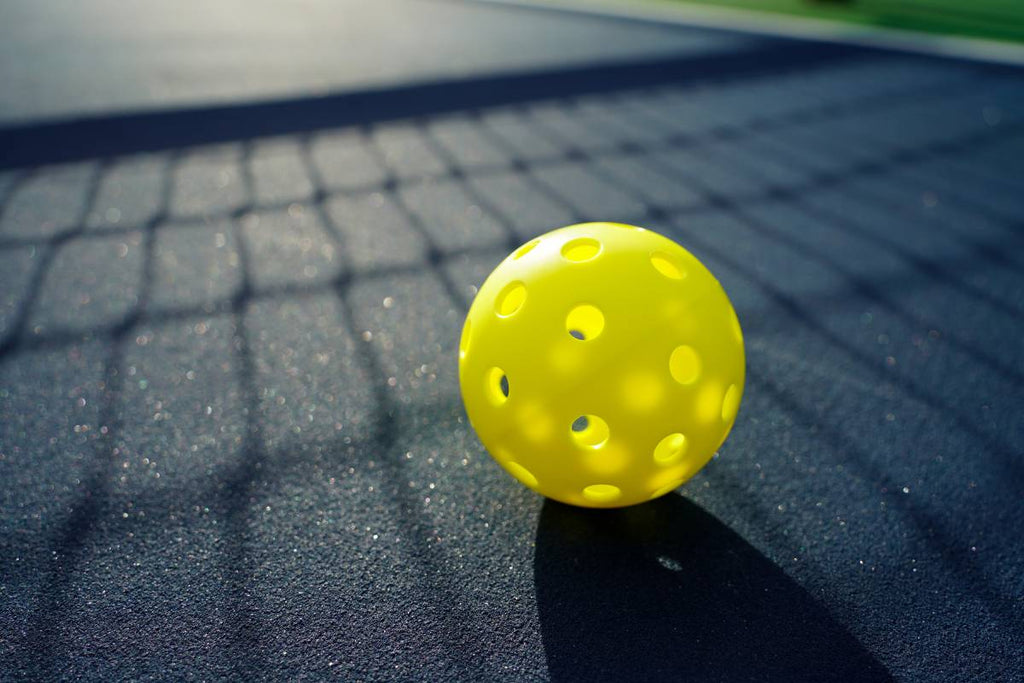A close-up view of a single pickleball sitting on a court.