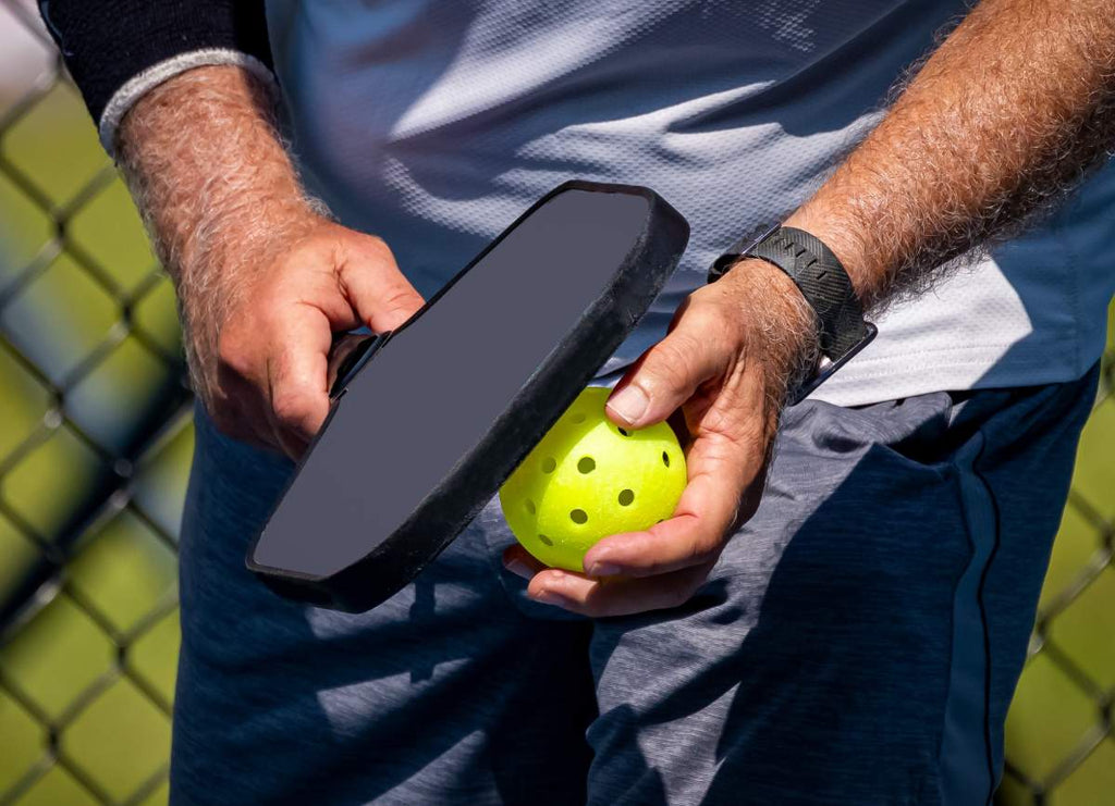 A pickleball player holds the ball before a serve.