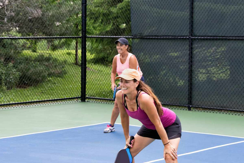 Two smiling players wait for their opponents to serve on a pickleball court.