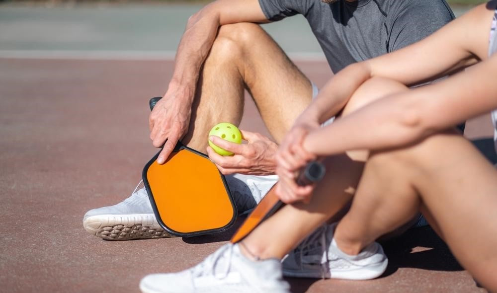 couple with pickleball paddle and board sitting in court