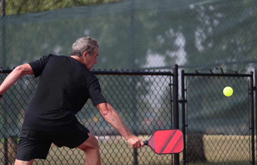 old man wearing black playing pickleball