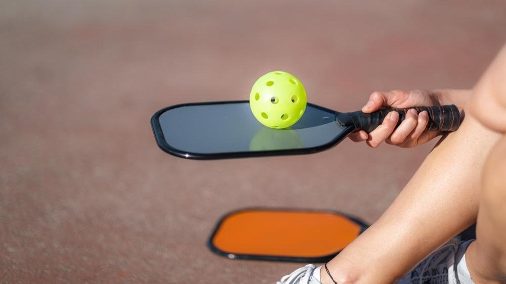 person with pickleball paddle and ball