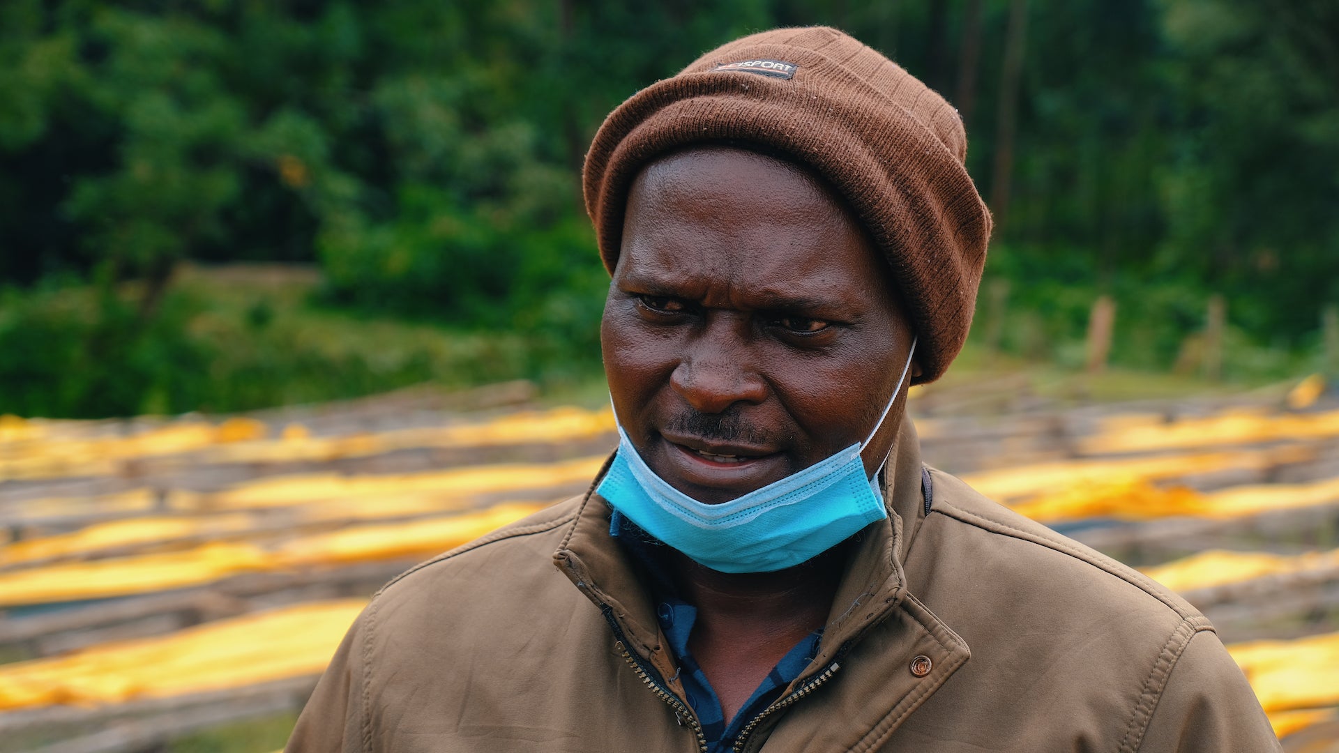 wideformat gentleman in front of coffee drying beds with bemused look on face.