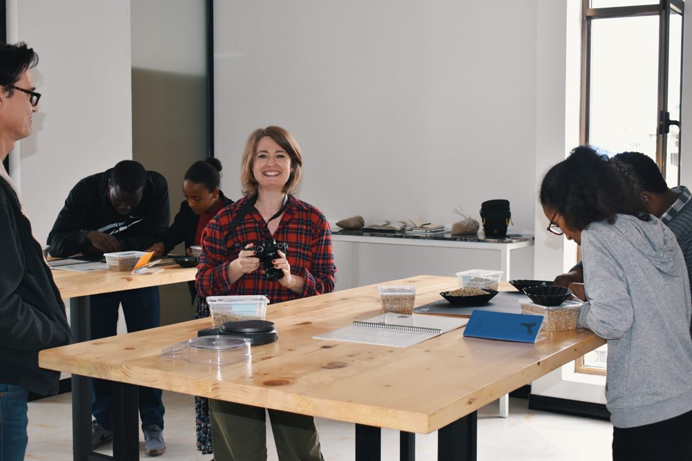 WideFormat Emily holding camera smiling in coffee lab in Addis Ababa, Ethiopia.