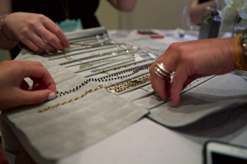 Photo of three hands picking up necklaces from a necklace roll from Sethi Couture.