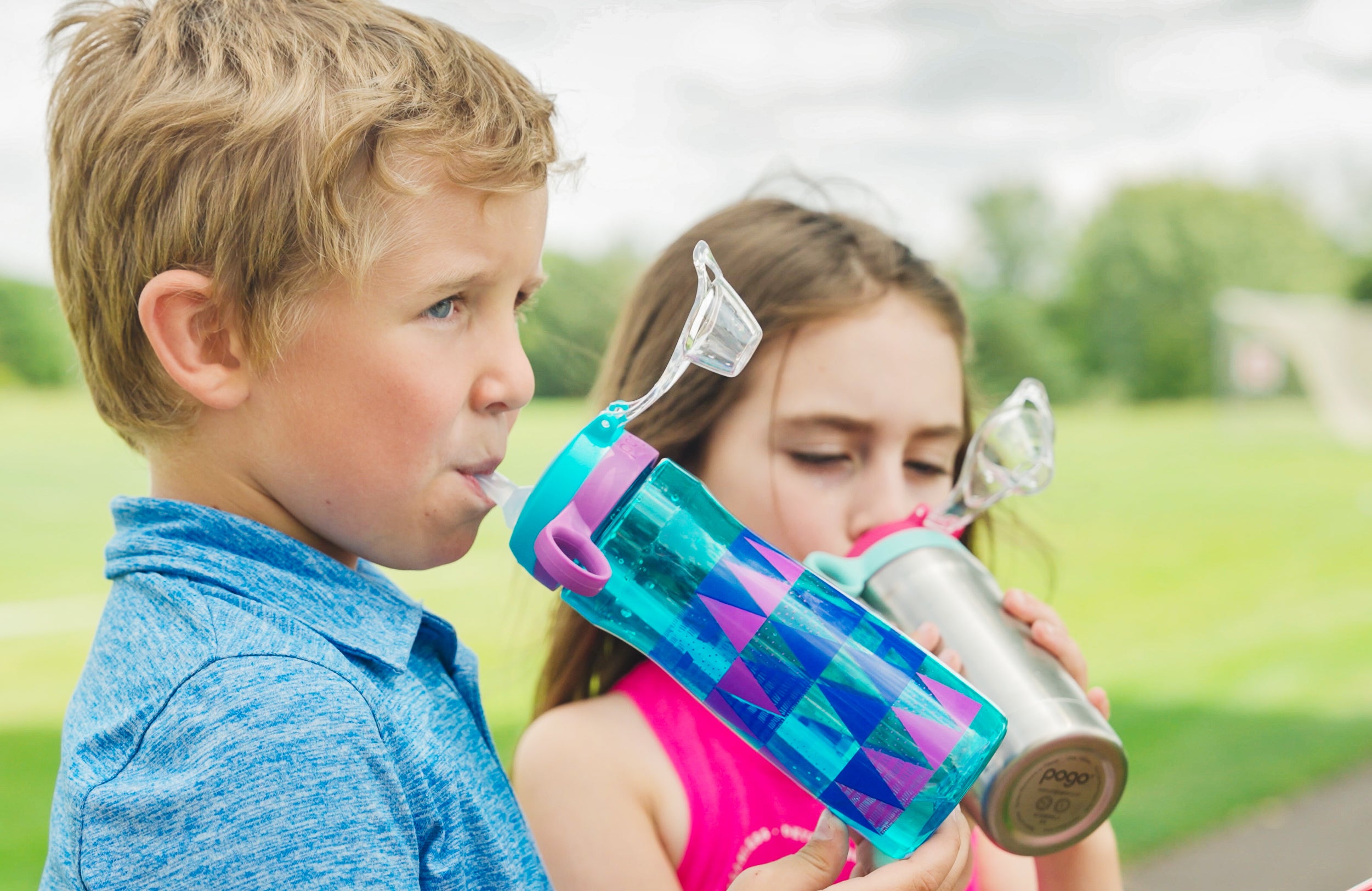 Children drinking from colorful water bottles outdoors.