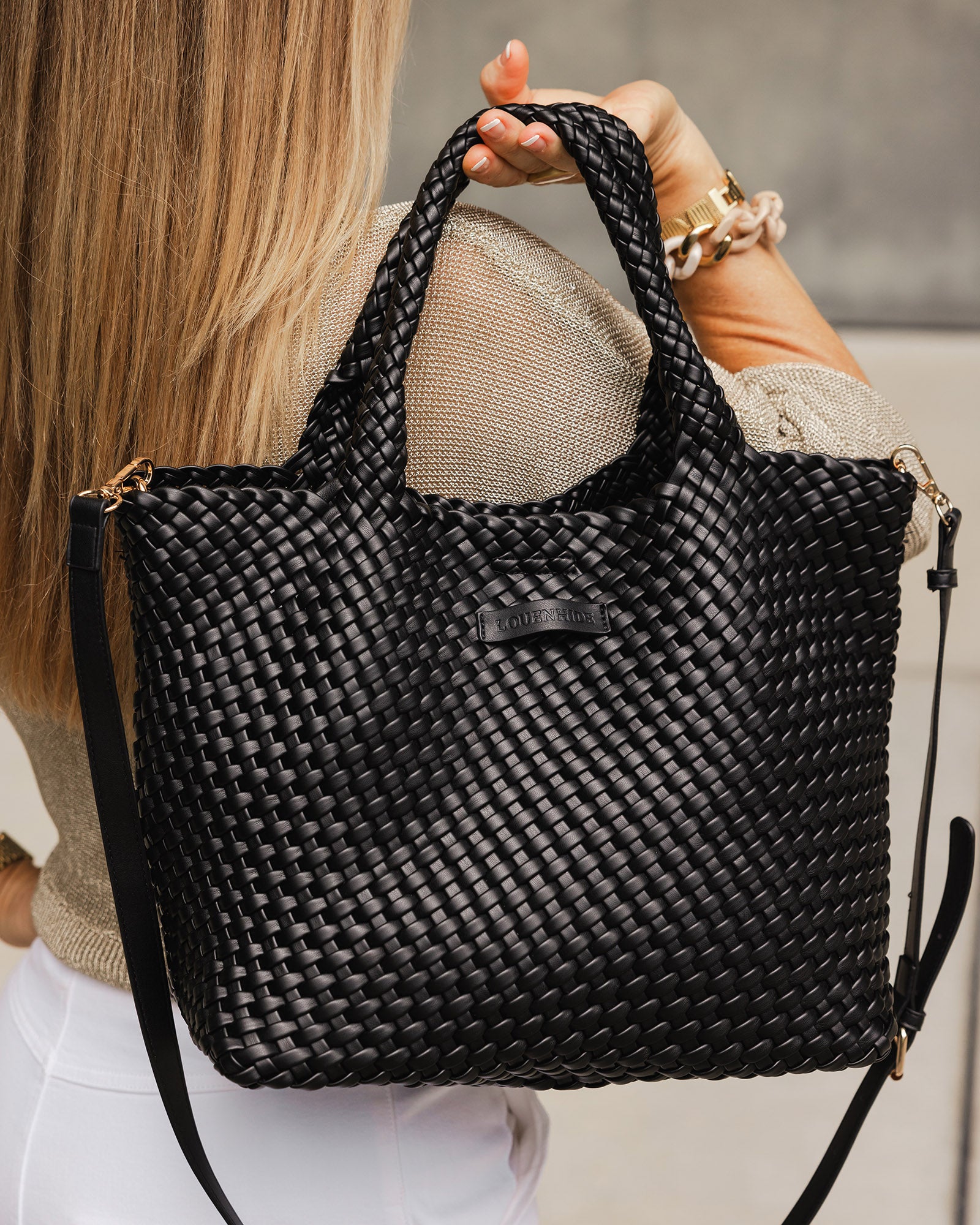 A woman wearing a gold lurex knit holding a black, woven tote bag by the handles