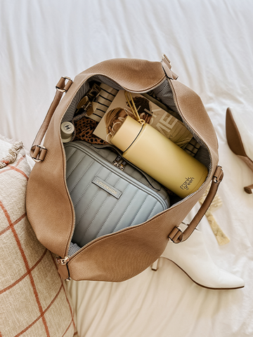 open camel coloured travel bag packed with clothes, waterbottle and cosmetic case