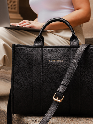 black handbag sitting next to woman with a laptop
