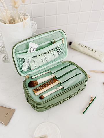 an opened sage green makeup bag filled with make up brushes and cosmetics