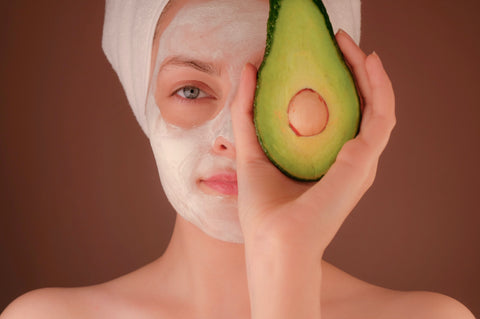 Photo of a woman with a face mask on, holding up an avocado. Photo taken by Kimia Zarifi.