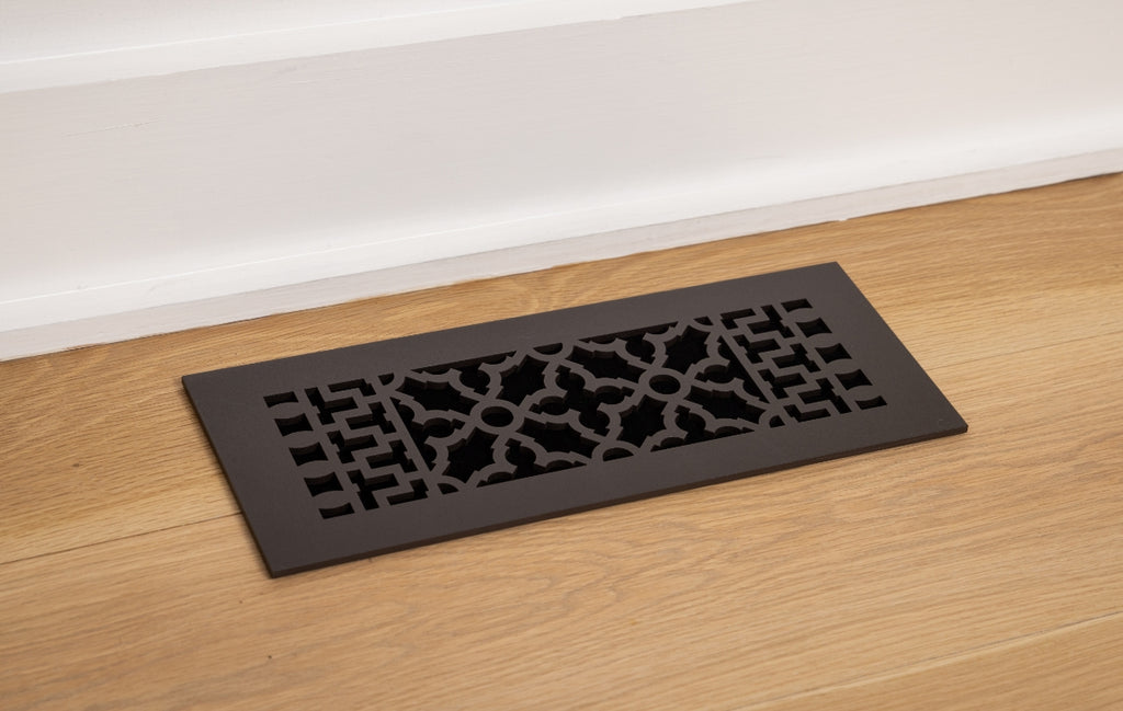 Installed cast iron register in a wood floor next to a white wall.