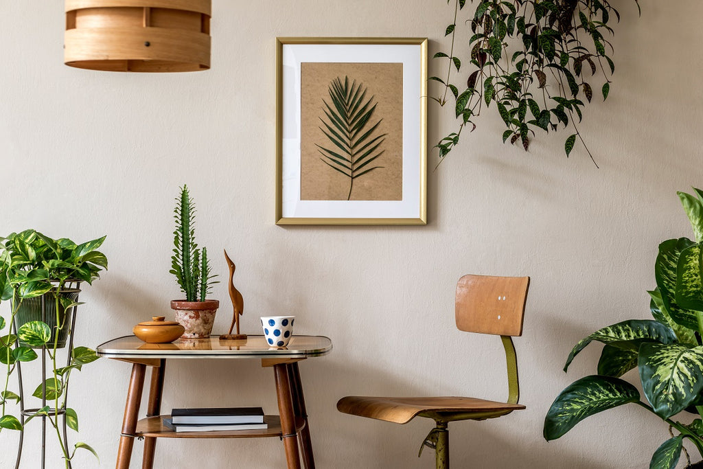 Small work space with a desk, plants, and art hung on the wall.