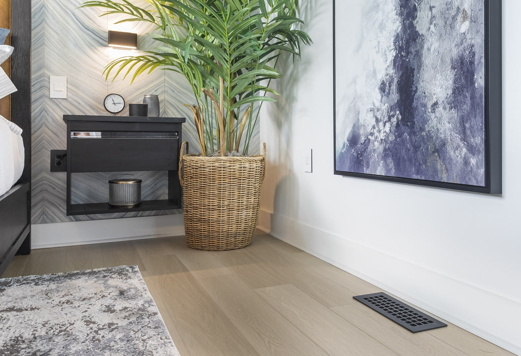 Corner of a living room with large art and plant plus a large vent cover in the floor.