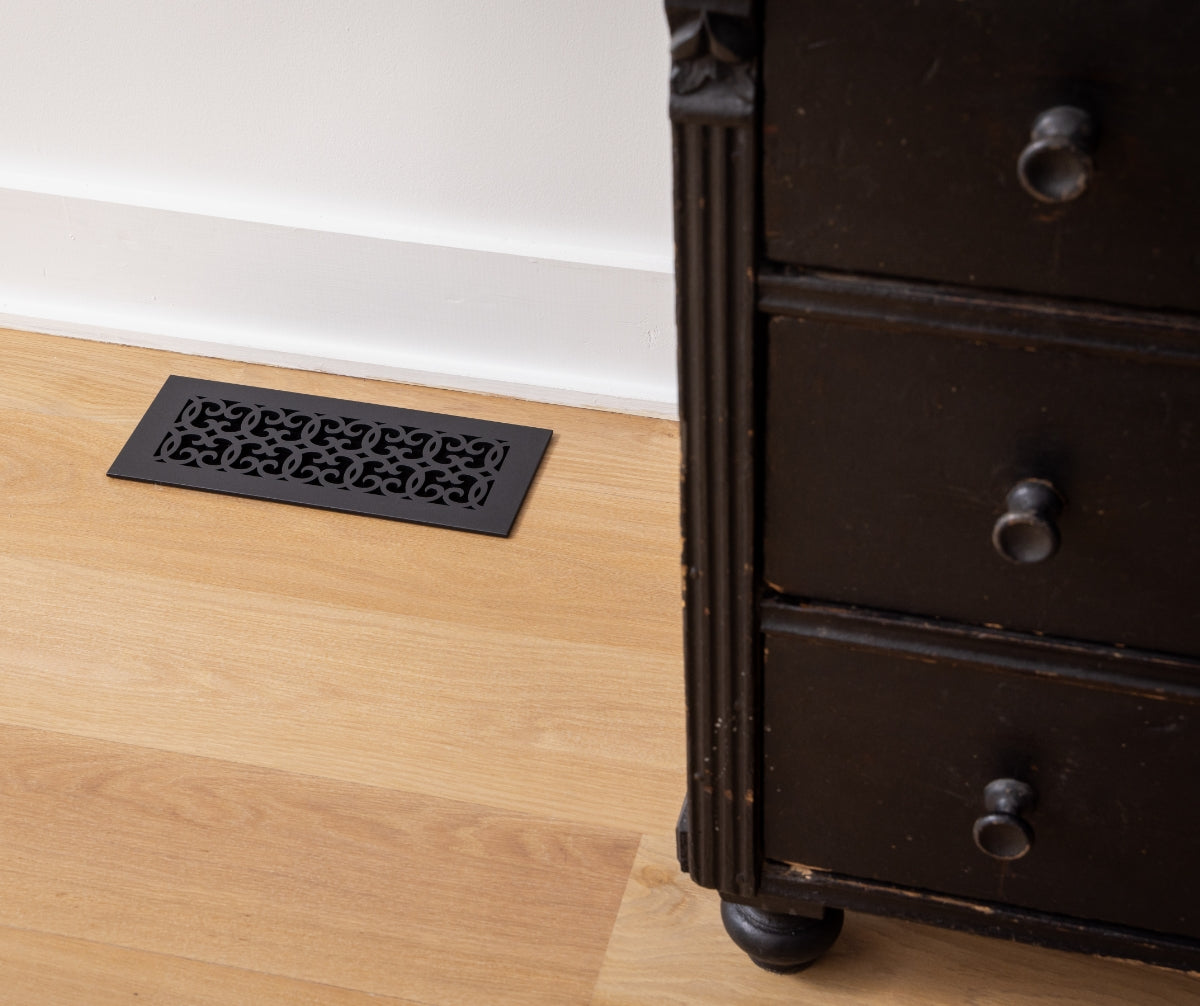 The Versaille pattern historic floor heating register in a light wood floor.