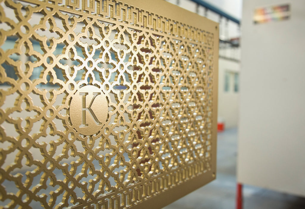 Custom made grille in gold with initial in the center of a scroll pattern.